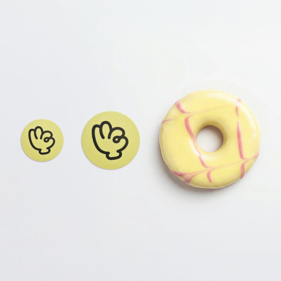 Two Suckers nipple stickers beside an iced doughnut, showing the size of the stickers by comparison